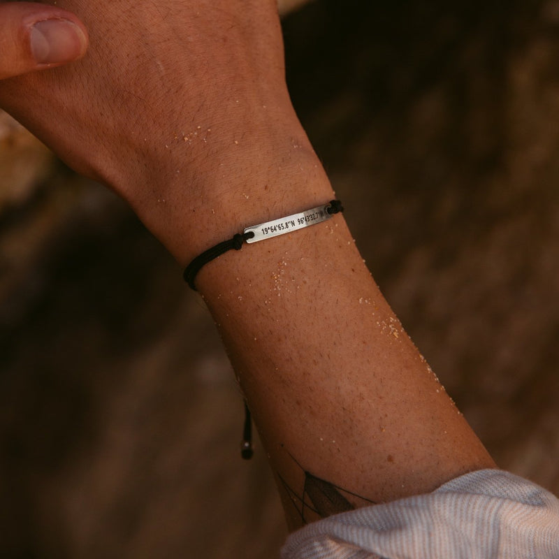 A man wearing a black thread bracelet with silver bar