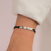 A woman wearing a black thread bracelet with a silver bar