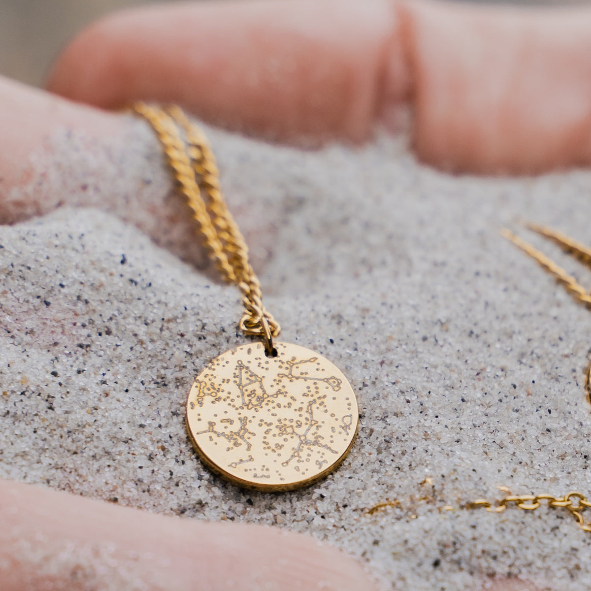 Gold necklace with a star constellation on sand