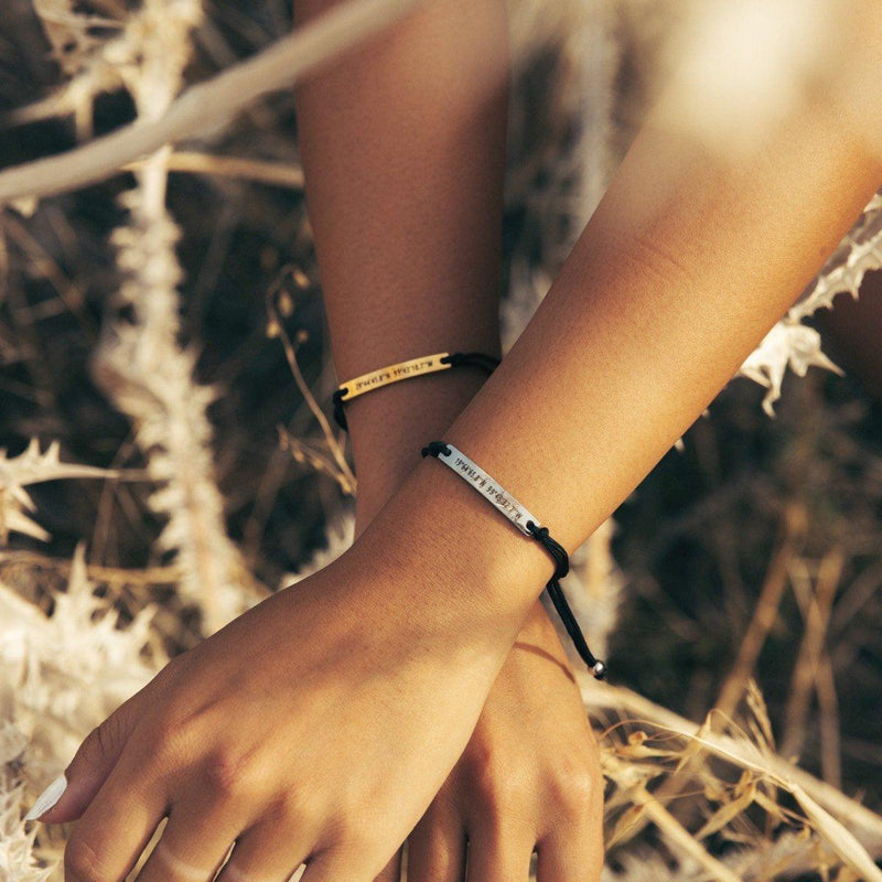 A black thread bracelet with gold bar and a black thread bracelet with silver bar